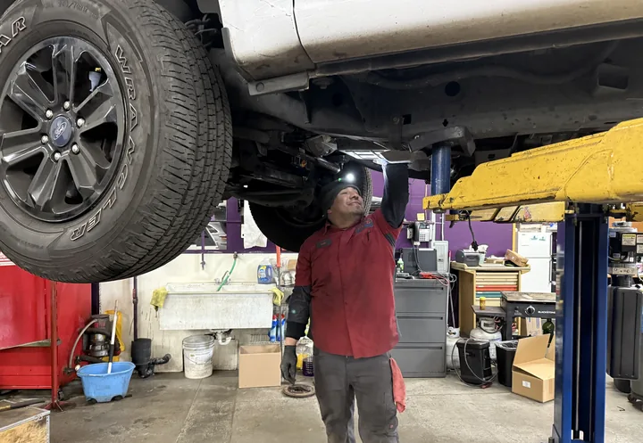 Luis inspecting the underside of a pickup truck on the lift with a flashlight